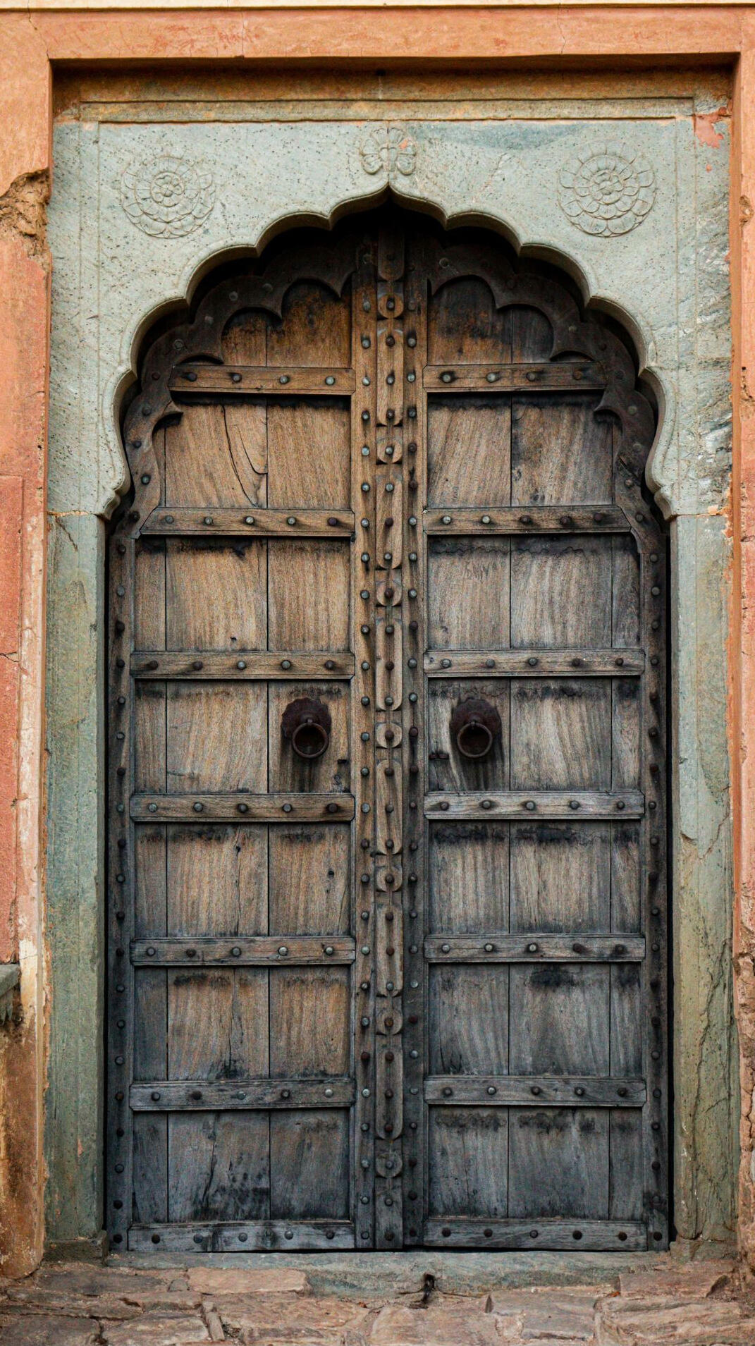 Ornate Wooden Haveli Door with Nine-Cusp Arch Old Indian haveli entrance with pale grey-green ochre surround, nine-cusp arch, and heavy double wooden doors studded with nails.