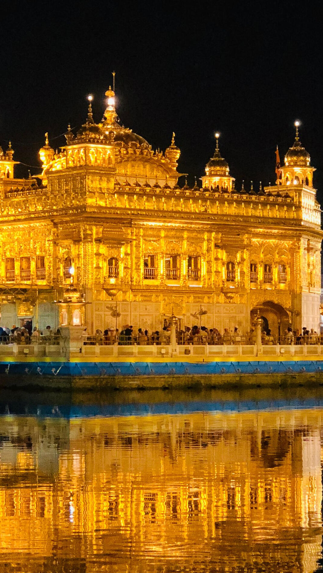 Close-up of the illuminated Golden Temple in Amritsar, India, with golden façade reflected in the sacred pond at night.